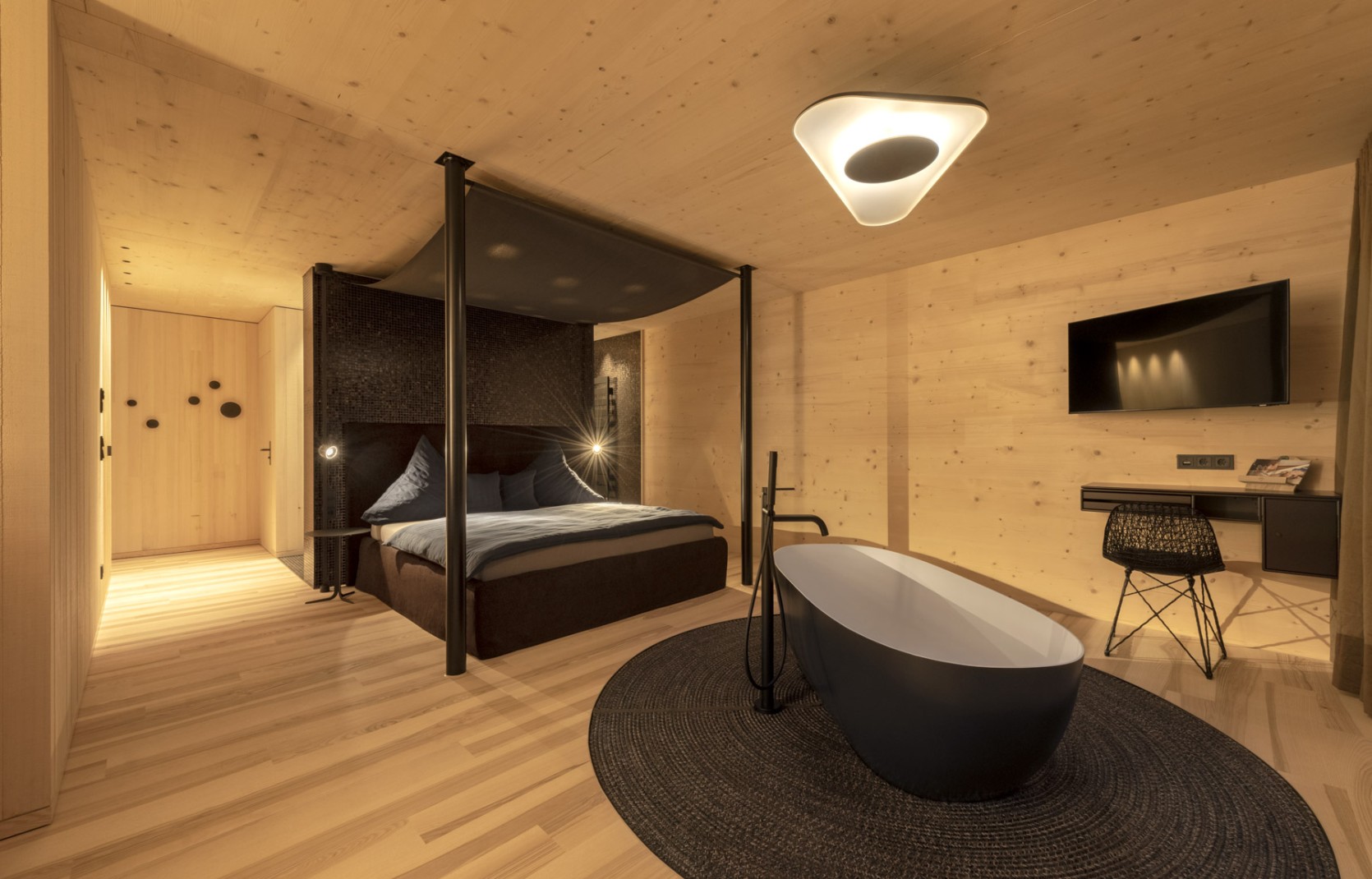 Stilvolles Zimmer im Hotel Oswalda Hus Kleinwalsertal mit einer freistehenden Badewanne, einem Himmelbett und hellen Holzwänden.
