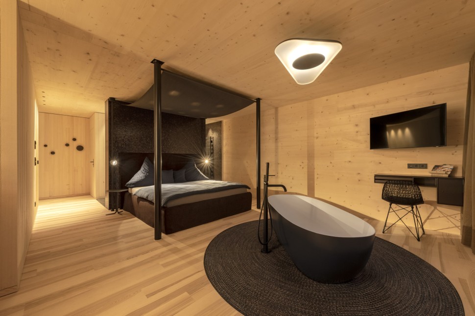 Stilvolles Zimmer im Hotel Oswalda Hus Kleinwalsertal mit einer freistehenden Badewanne, einem Himmelbett und hellen Holzwänden.