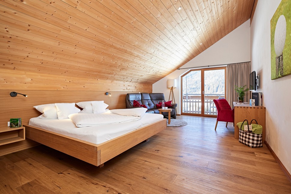 Hotelzimmer im Dachgeschoss mit Holzwänden, Balkon und Sofa im Oswalda Hus Hotel Kleinwalsertal.