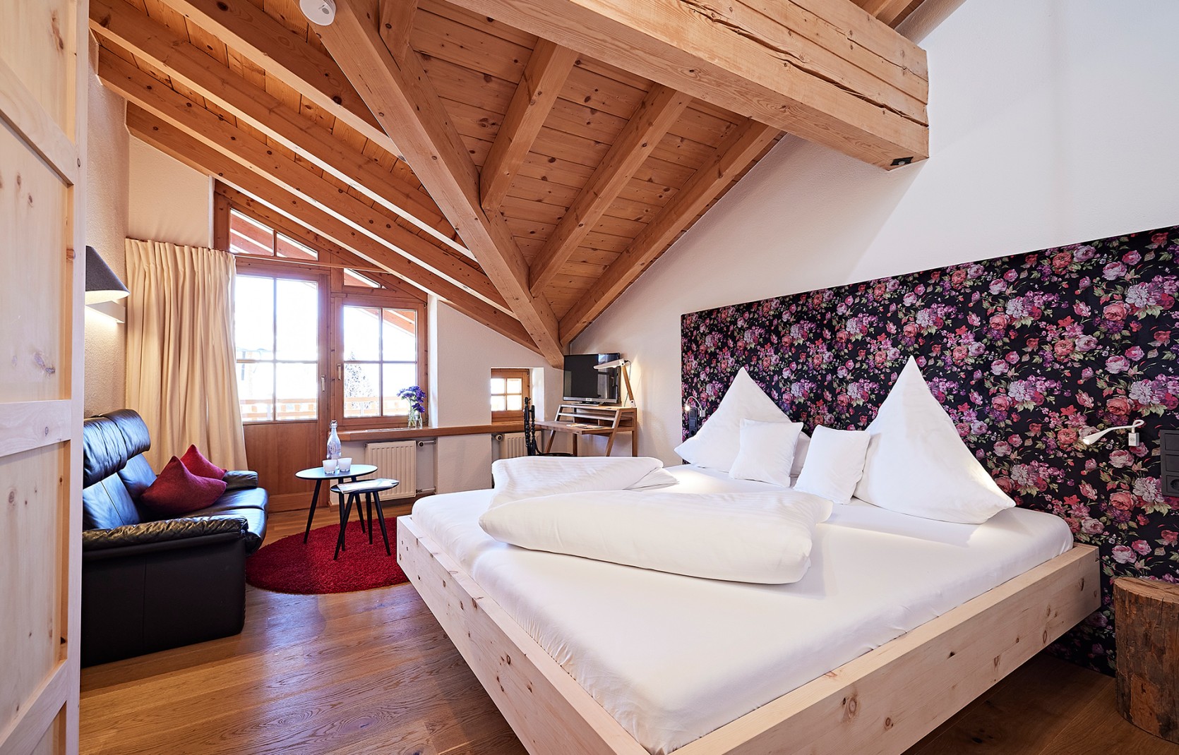 Hotelzimmer mit Dachschräge, Sofa, Balkon und geblümter Tapete im 4 Sterne Hotel Oswalda Hus im Kleinwalsertal.