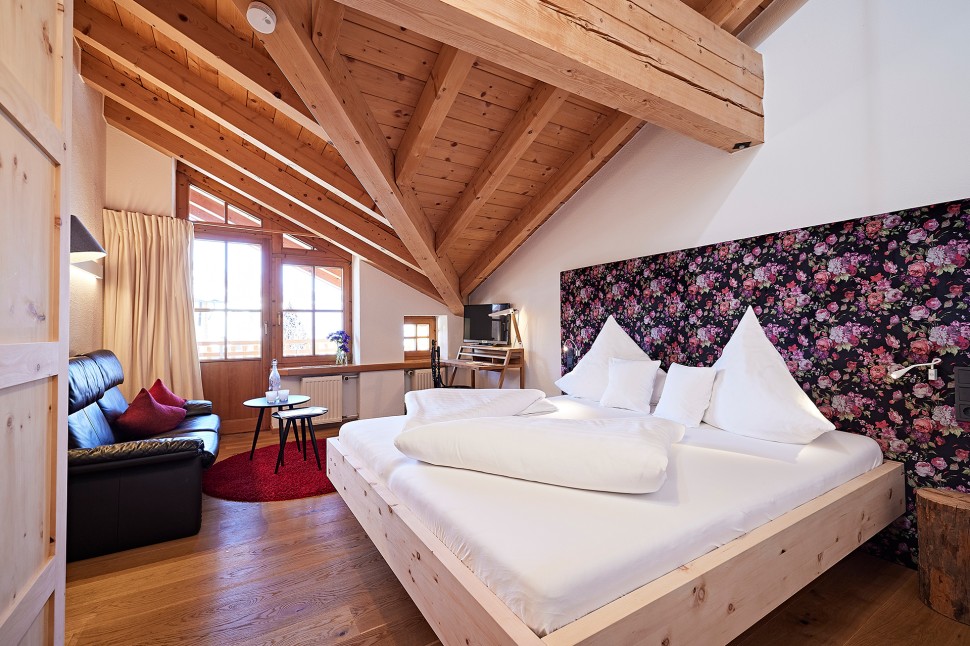 Hotelzimmer mit Dachschräge, Sofa, Balkon und geblümter Tapete im 4 Sterne Hotel Oswalda Hus im Kleinwalsertal.