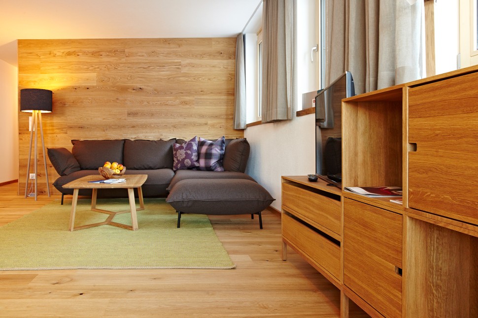 Ferienwohnung mit Sofa, Holzwand und grünem Teppich im Oswalda Hus Kleinwalsertal.