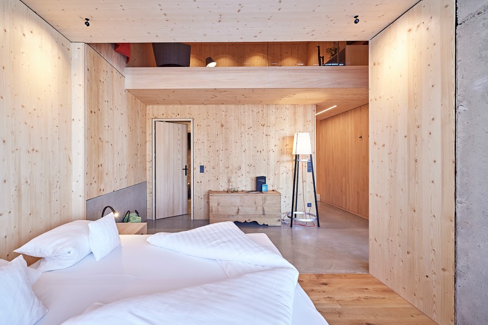 Schlichtes Hotelzimmer mit Holzwänden, Sichtbeton und roten Vorhängen im 4 Sterne Hotel Oswalda Hus im Kleinwalsertal.