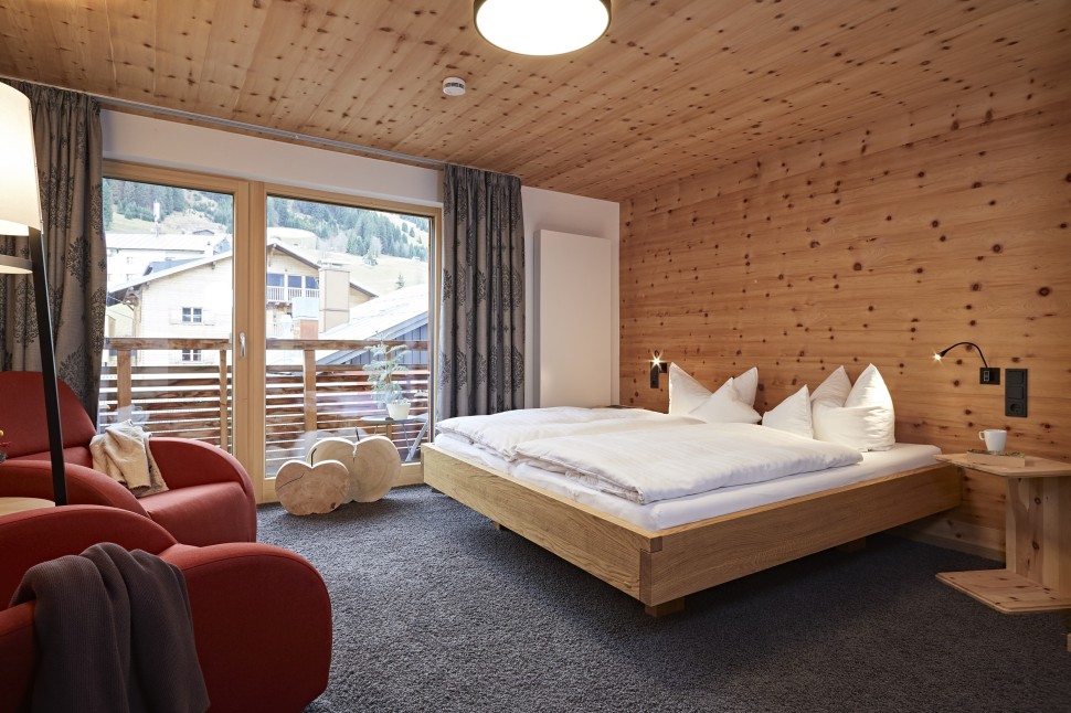 Geräumiges Hotelzimmer mit Balkon, Sitzecke, Schreibtisch und Holzwänden im 4 Sterne Hotel Oswalda Hus Kleinwalsertal.