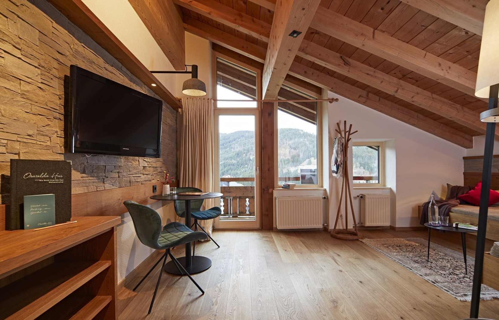 Hotelzimmer im Dachgeschoss mit Holzwänden, Balkon und Sofa im Oswalda Hus Hotel Kleinwalsertal.