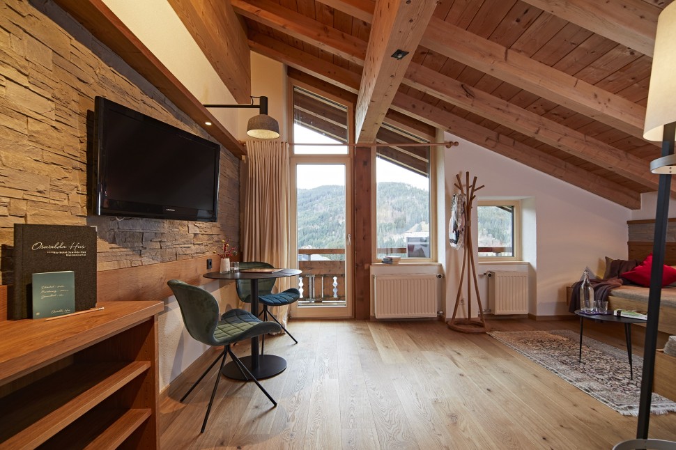 Hotelzimmer im Dachgeschoss mit Holzwänden, Balkon und Sofa im Oswalda Hus Hotel Kleinwalsertal.