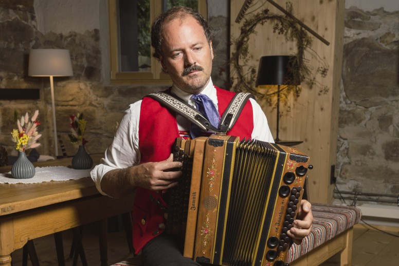 Mann in Tracht beim musizieren auf einer Ziehharmonika im 4 Sterne Hotel Kleinwalsertal als Symbol für Tradition im Oswalda Hus.
