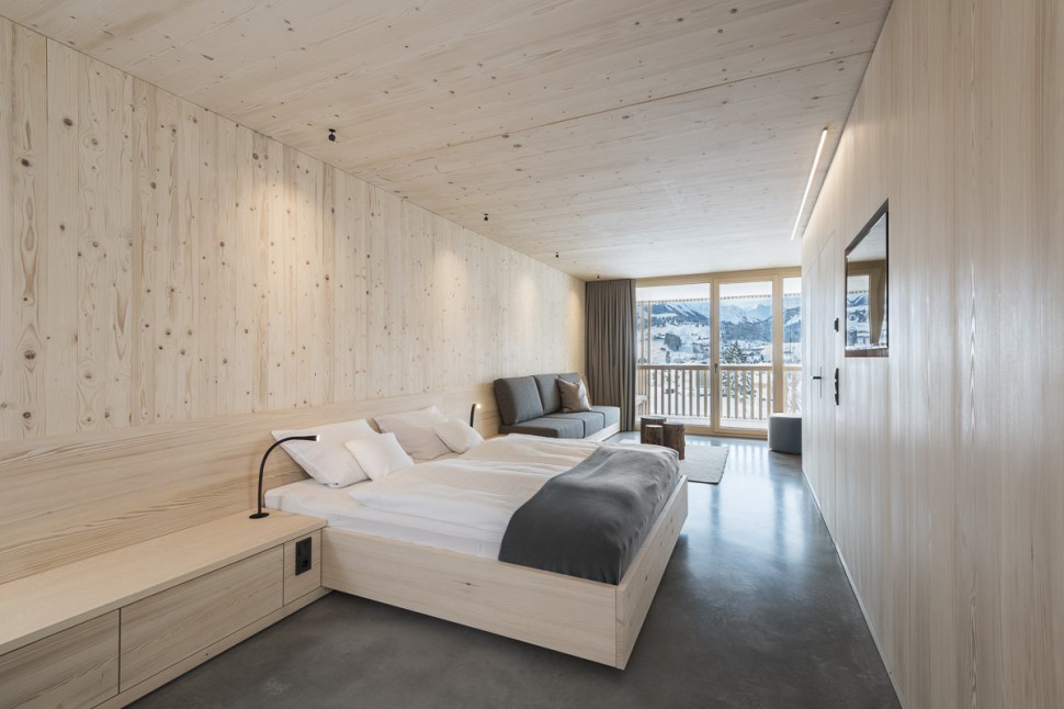 Schlichtes Hotelzimmer mit Holzwänden, Sichtbeton und grauen Vorhängen im 4 Sterne Hotel Oswalda Hus im Kleinwalsertal.