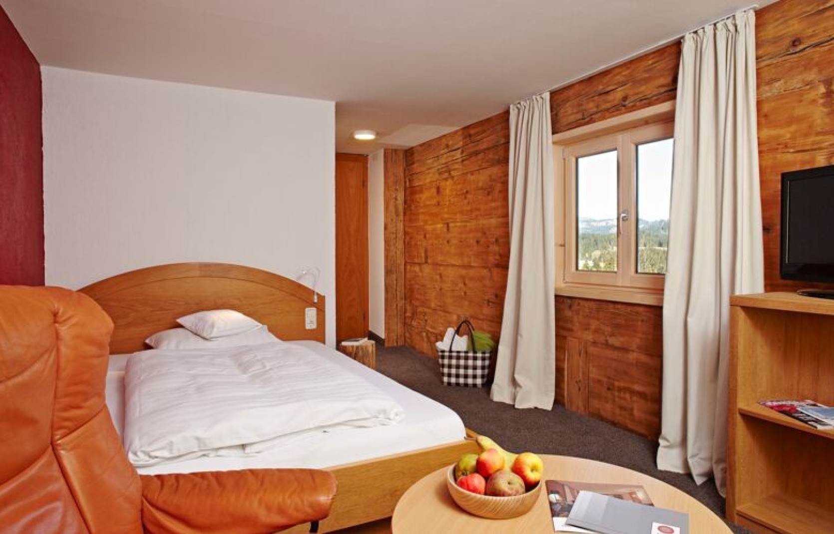 Einzelzimmer mit historischer Holzwand, Ledersessel und großem Bett im Kleinwalsertal Hotel Oswalda Hus.