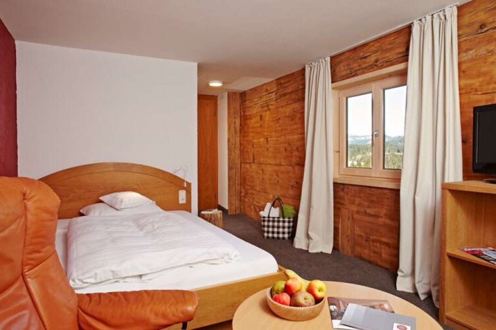 Einzelzimmer mit historischer Holzwand, Ledersessel und großem Bett im Kleinwalsertal Hotel Oswalda Hus.