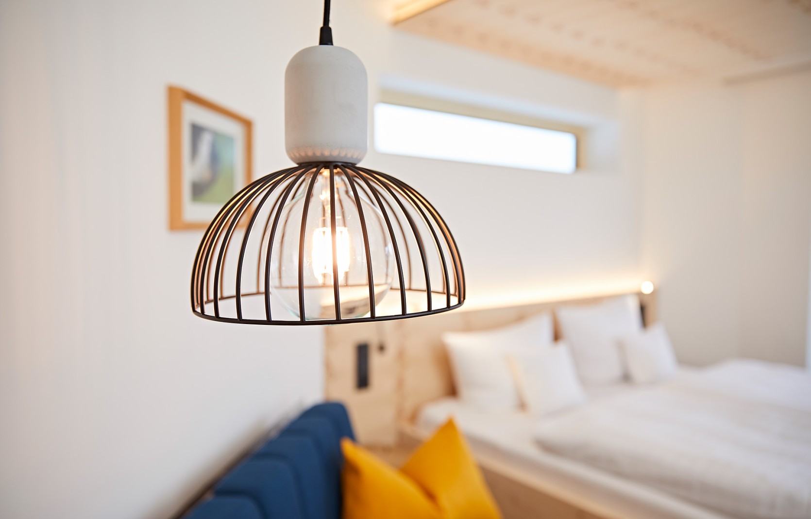 Modernes Hotelzimmer mit blauem Sofa, Beleuchtung, Fernseher und Balkon in hellen Holzfarben im Kleinwalsertal Hotel Oswalda Hus.