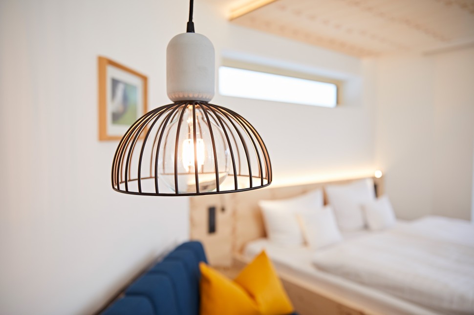 Modernes Hotelzimmer mit blauem Sofa, Beleuchtung, Fernseher und Balkon in hellen Holzfarben im Kleinwalsertal Hotel Oswalda Hus.