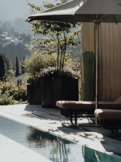 Wellnesshotel im Kleinwalsertal mit Außenpool, Sonnenliegen, Sonnenschirm und Sträuchern im Oswalda Hus.