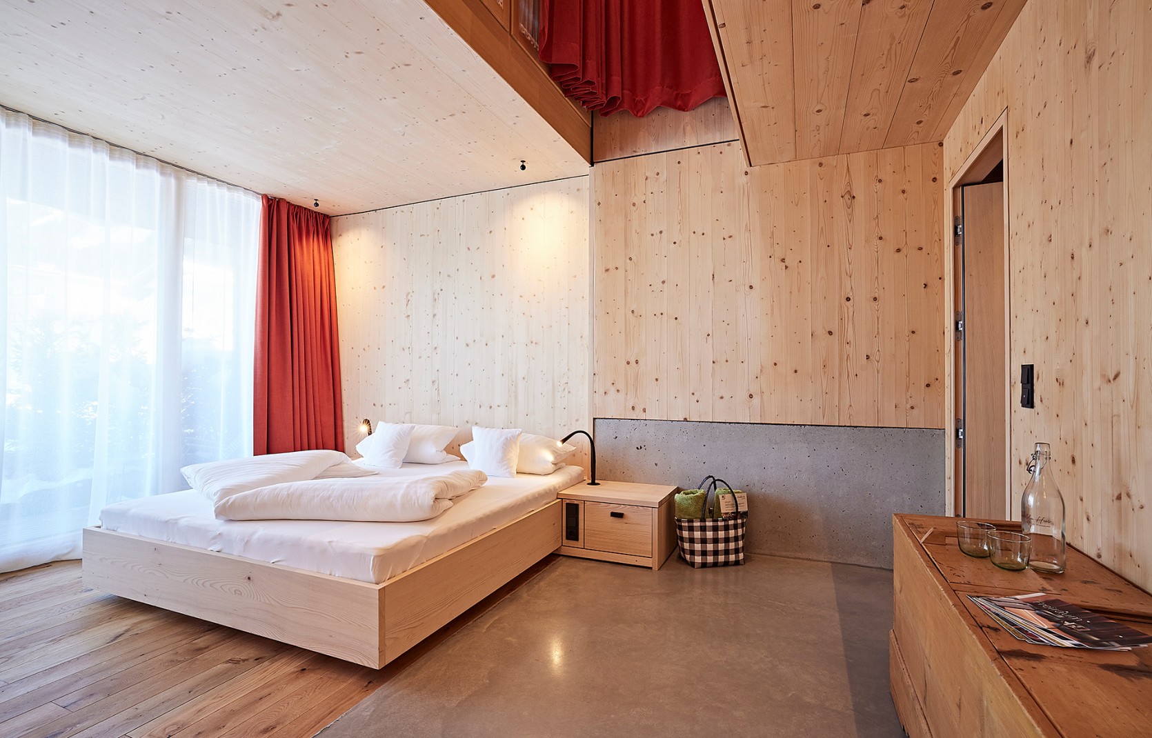 Schlichtes Hotelzimmer mit Holzwänden, Sichtbeton und roten Vorhängen im 4 Sterne Hotel Oswalda Hus im Kleinwalsertal.