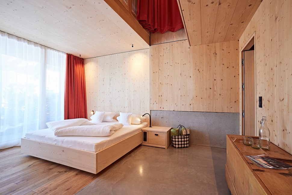 Schlichtes Hotelzimmer mit Holzwänden, Sichtbeton und roten Vorhängen im 4 Sterne Hotel Oswalda Hus im Kleinwalsertal.