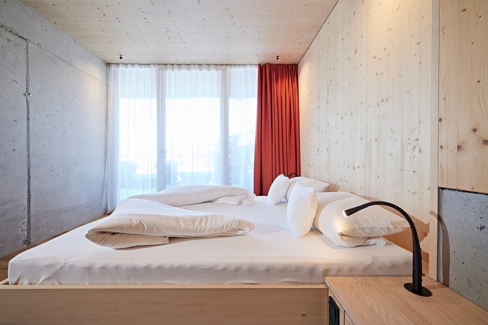 Schlichtes Hotelzimmer mit Holzwänden, Sichtbeton und roten Vorhängen im 4 Sterne Hotel Oswalda Hus im Kleinwalsertal.