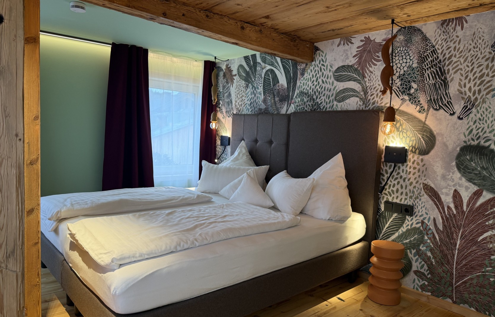 Schlafzimmer mit gemusterter Tapete und Polsterbett im Oswalda Hus Ferienhaus Kleinwalsertal.
