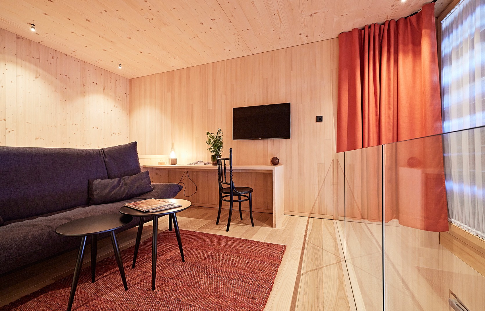 Schlichtes Hotelzimmer mit Holzwänden, Sichtbeton und roten Vorhängen im 4 Sterne Hotel Oswalda Hus im Kleinwalsertal.