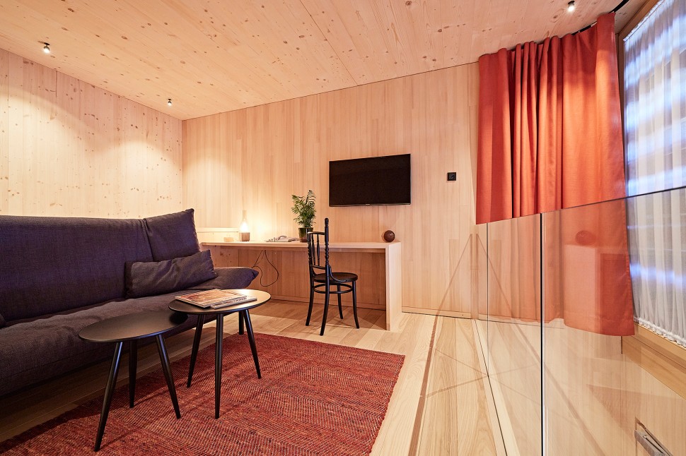 Schlichtes Hotelzimmer mit Holzwänden, Sichtbeton und roten Vorhängen im 4 Sterne Hotel Oswalda Hus im Kleinwalsertal.
